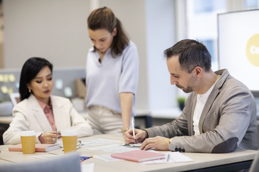 Trois personnes collaborant autour d'une table dans un bureau, concentrées sur leur travail.